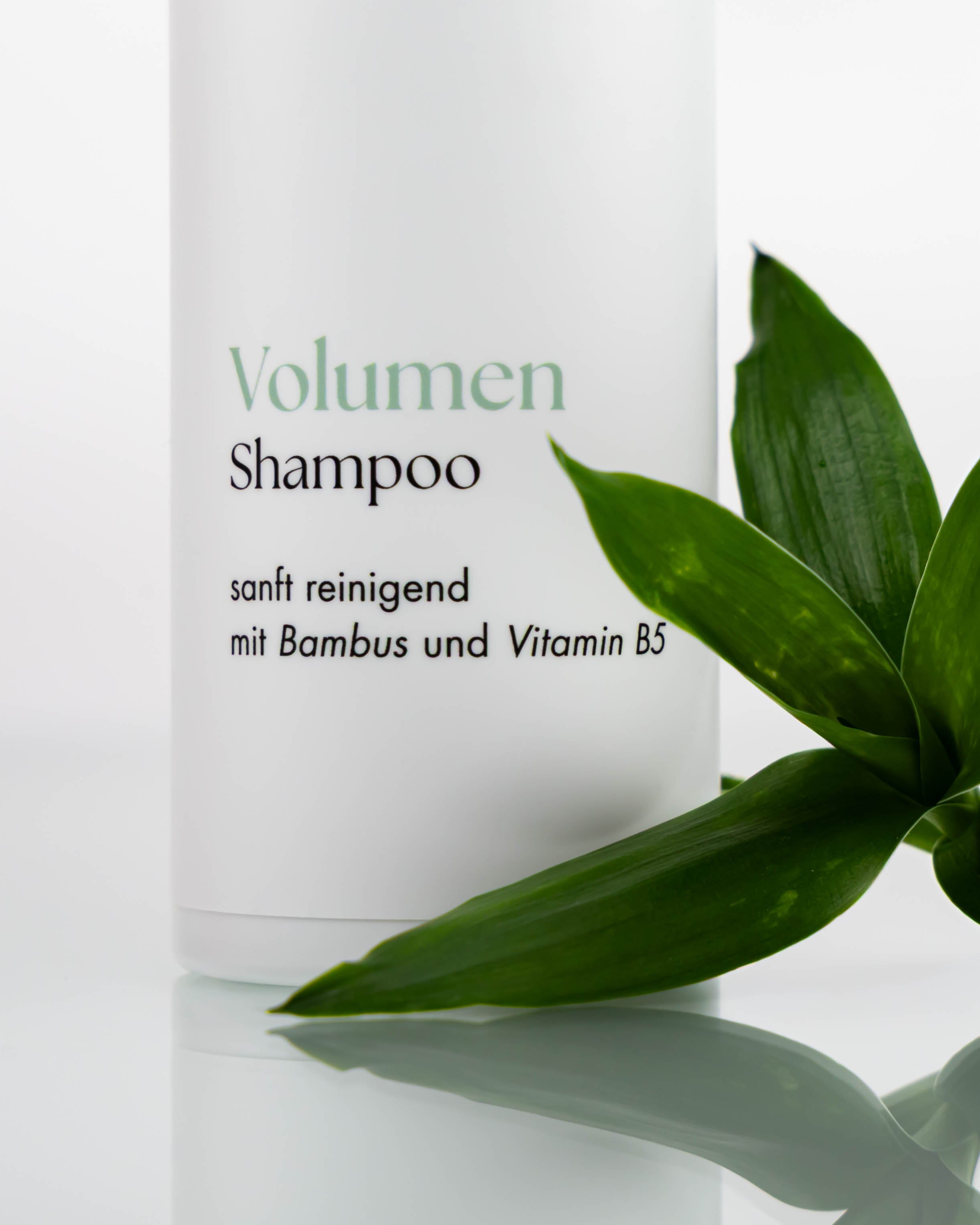 Flasche Volumenshampoo, neben ihr liegen Bambusblätter.